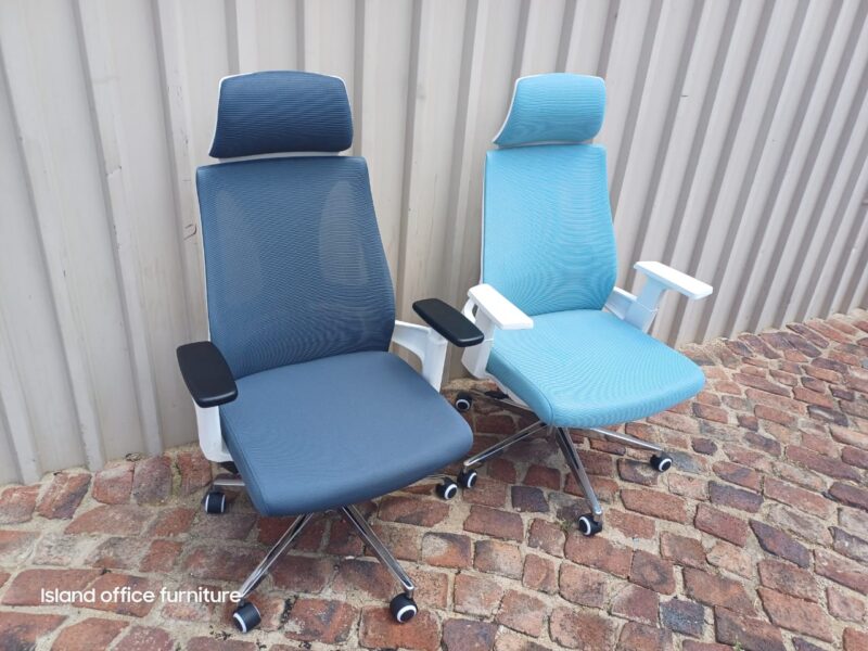 Two Moritz Ergonomic Grey Chairs with headrests and 3D armrests, displayed against a corrugated wall.